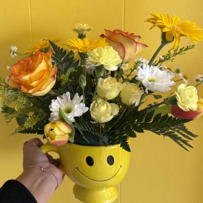 Bouquet of yellow and orange flowers in a smiley-face mug