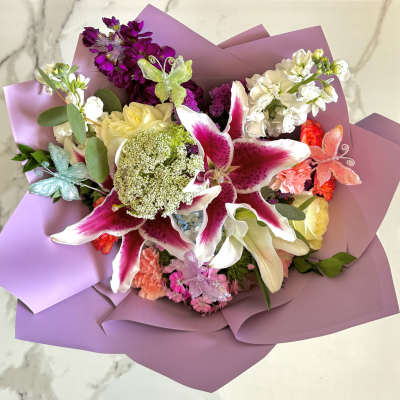 Bouquet of pink lilies, white roses, and purple flowers wrapped in lavender paper