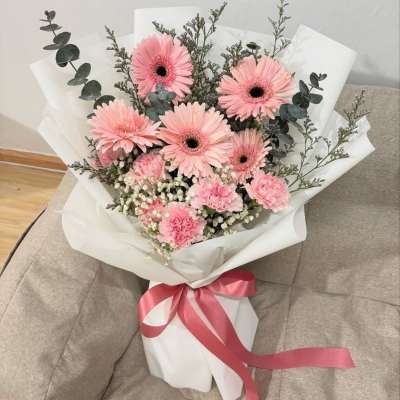 Pink gerbera daisy bouquet wrapped in white paper with a pink ribbon