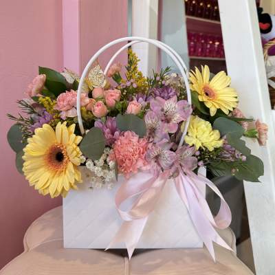 Pastel flower arrangement in a white gift bag with pink ribbon
