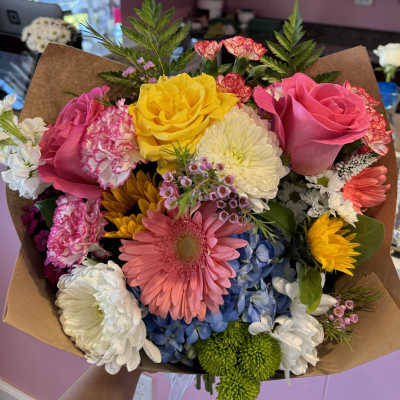 Colorful mixed bouquet with roses, gerbera daisies, and chrysanthemums wrapped in brown paper