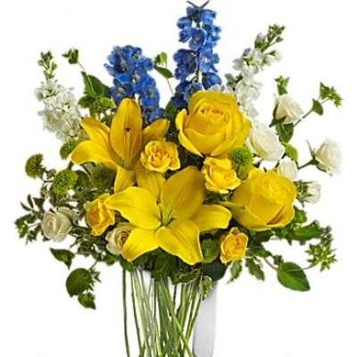 Yellow lilies and roses in a clear glass vase with blue and white flowers