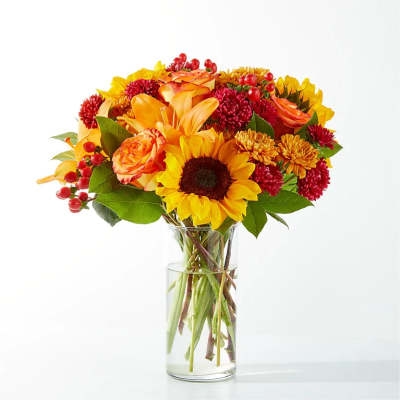 Bouquet of sunflowers, orange roses, and red mums in a clear glass vase