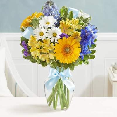 Mixed bouquet of daisies, gerberas, and blue flowers in a glass vase