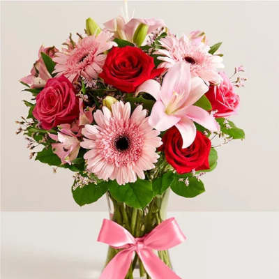Pink and red flower bouquet in a glass vase with a pink ribbon