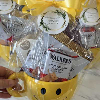 Gift basket in a yellow smiley-face mug with wrapped snacks and a ribbon
