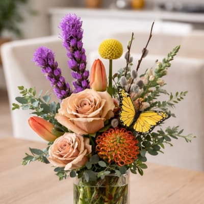 Mixed bouquet in a clear glass vase with roses, tulips, and a butterfly accent