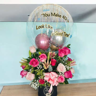 Pink rose arrangement with a clear balloon and metallic balloons in a black box