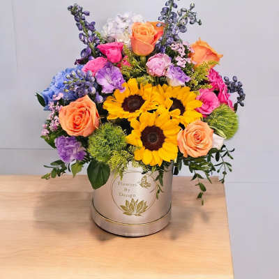 Colorful mixed bouquet in a round hatbox with sunflowers and roses