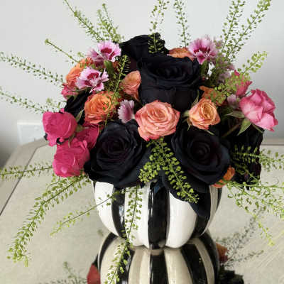 Black and peach roses with pink blooms in a striped vase arrangement
