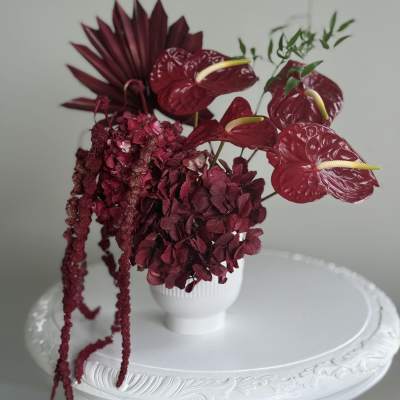 Deep burgundy floral arrangement in a white vase with hanging blooms
