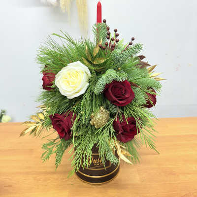 Holiday arrangement of red and white roses in a black container with a red candle