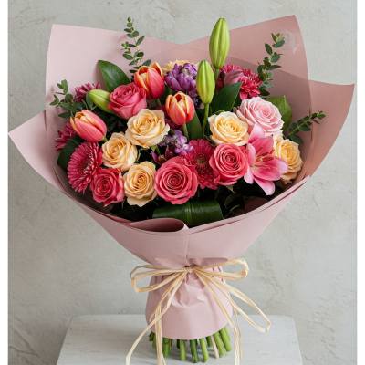 Pink and peach bouquet with roses, tulips, lilies, and chrysanthemums wrapped in blush paper