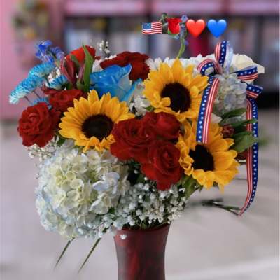 Bouquet of sunflowers and red roses in a red vase with patriotic ribbon