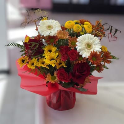 Bouquet of red roses, white gerbera daisies, and yellow mums in pink wrap