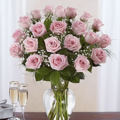 Tall arrangement of light pink roses with white filler flowers in a clear glass vase on a table