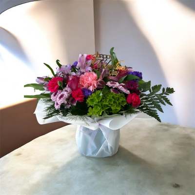 Mixed pink and purple bouquet in a wrapped vase with a Valentine’s Day topper