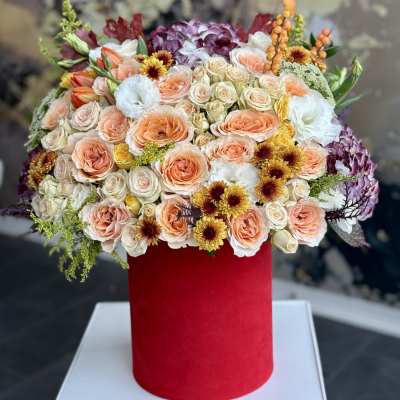 Mixed bouquet of peach, cream, and purple flowers in a red cylindrical box