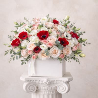 Bouquet of pale roses and red anemones in a white box