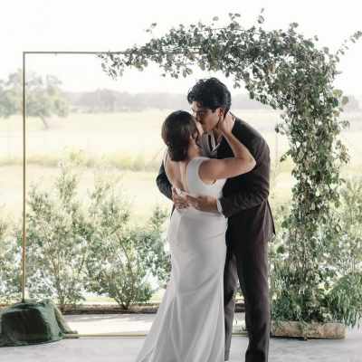 Couple kissing beneath a leafy wedding arch