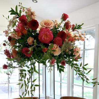 Tall floral arrangement with pink, peach, and red blooms in a room by windows