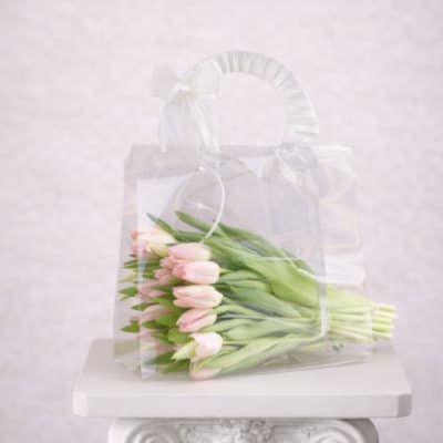 A wrapped bouquet of pale pink tulips in a clear gift bag