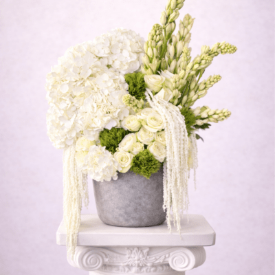Tall white and green floral arrangement with hydrangeas and roses in a gray pot on a pedestal.