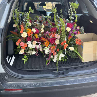 Car trunk filled with colorful mixed flower arrangements and boxes