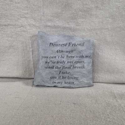 Square gray memorial stone with engraved poem text on a neutral fabric background