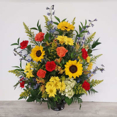 Tall arrangement of sunflowers, yellow daisies, orange roses and red carnations in a dark vase