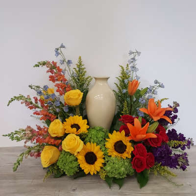 Cremation urn surrounded by bright yellow sunflowers, roses, orange lilies, and mixed colorful flowers