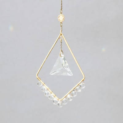 Geometric gold hanging ornament with clear crystal prism and beads on a gray background