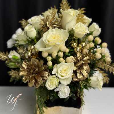 White roses in a gold-toned square vase with gold pinecones