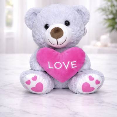 Gray teddy bear holding a pink heart with the word LOVE
