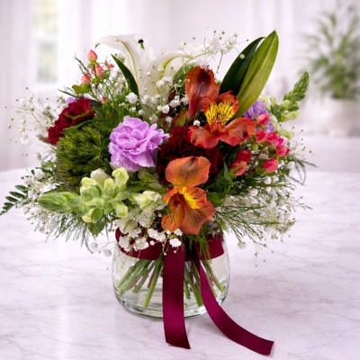 Mixed bouquet in a clear glass vase with a burgundy ribbon