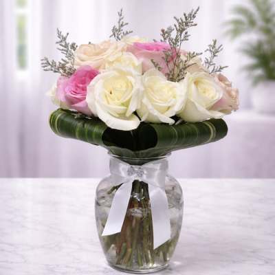 Pink and white roses arranged in a glass vase with a white ribbon
