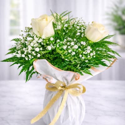 Bouquet of white roses and baby's breath wrapped in white paper with a gold ribbon