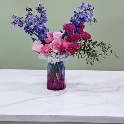 Pink and purple flower arrangement in a purple glass vase