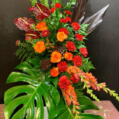 Tropical floral arrangement with orange roses, red carnations, and large monstera leaves