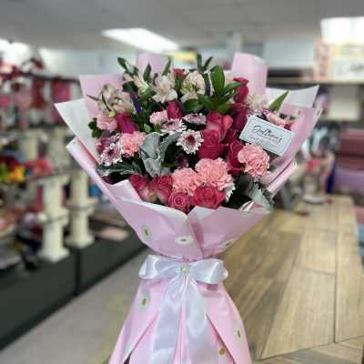 Pink bouquet of roses, carnations, and small daisy-like flowers wrapped in pink paper