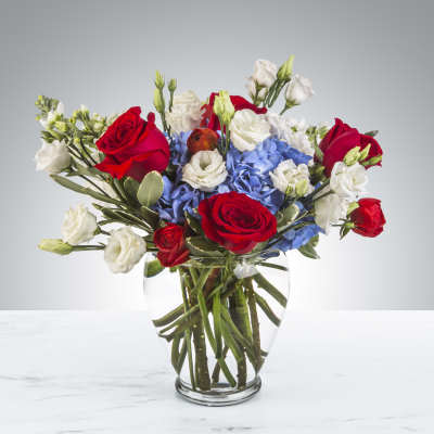 Red roses, white lisianthus, and blue hydrangeas arranged in a clear glass vase