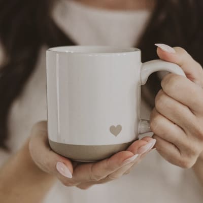 Hands holding a white ceramic mug with a small heart detail