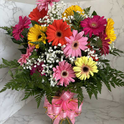 Colorful gerbera daisy bouquet in a glass vase with a pink ribbon