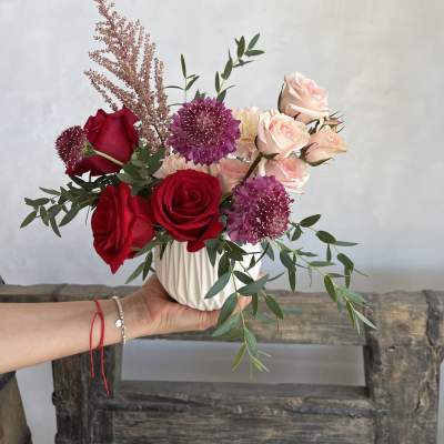 Bouquet of red and blush roses with purple blooms in a white vase
