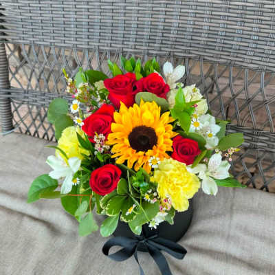 Bouquet of red roses, a sunflower, and yellow carnations in a black box