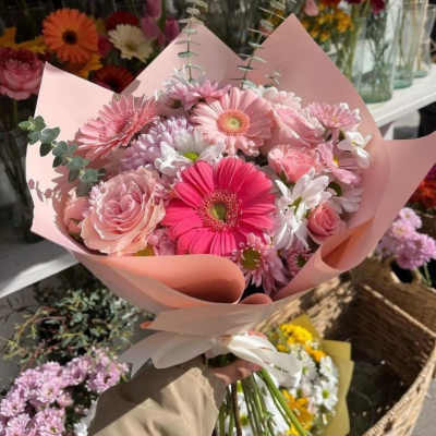 Pink bouquet of gerbera daisies, roses, and chrysanthemums wrapped in blush paper