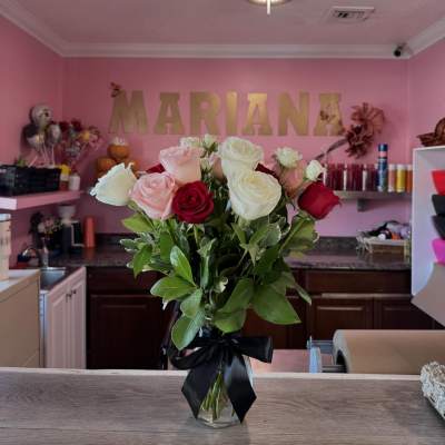Bouquet of pink, white, and red roses in a glass vase with a black ribbon