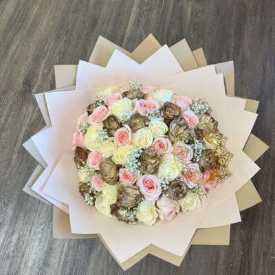 Round bouquet of pink, cream, and brown roses wrapped in layered paper