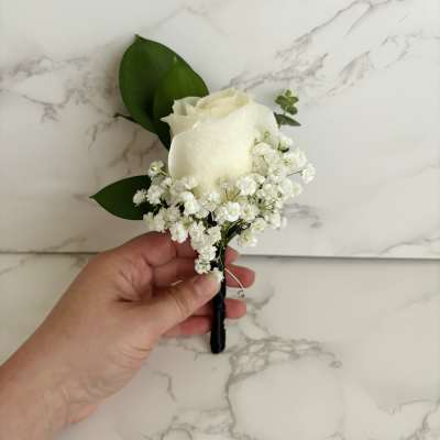 White rose boutonniere with baby's breath and green leaves