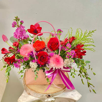 Pink and red mixed flower arrangement in a pink handled box with ribbon